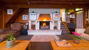 A cozy living room with a fireplace, wooden ceiling, and a staircase leading to another level.