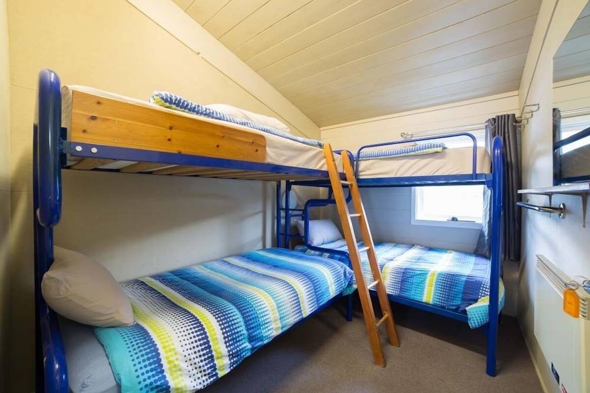 A bunk bed room with two beds, a ladder, and a window.