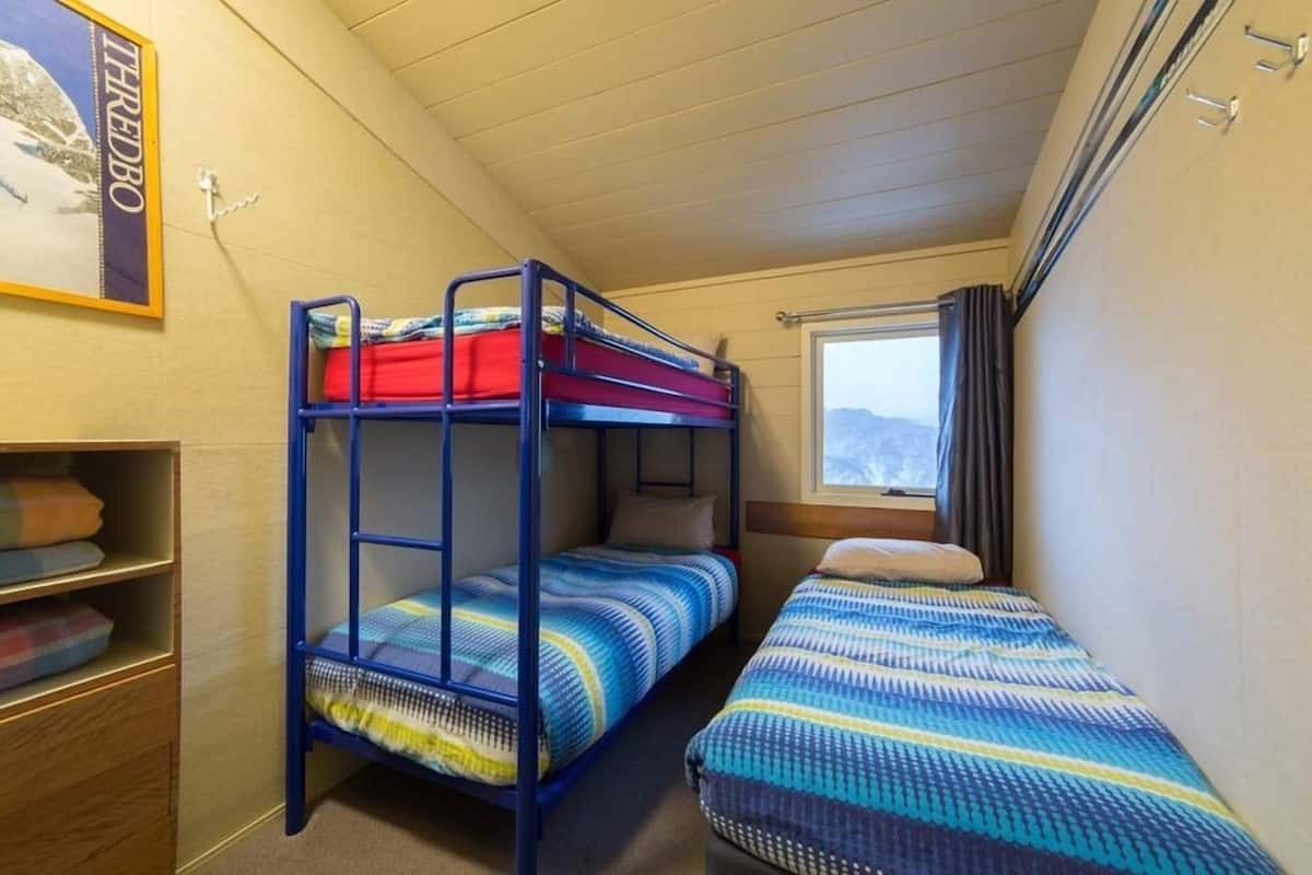 A bunk bed room with a window and a shelf with folded blankets.