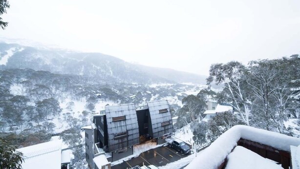 A modern building with a parking area and a view of snow-covered hills.