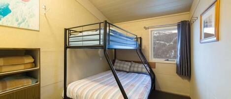 Een slaapkamer met een stapelbed, een raam, een schilderij aan de muur en een houten kast.