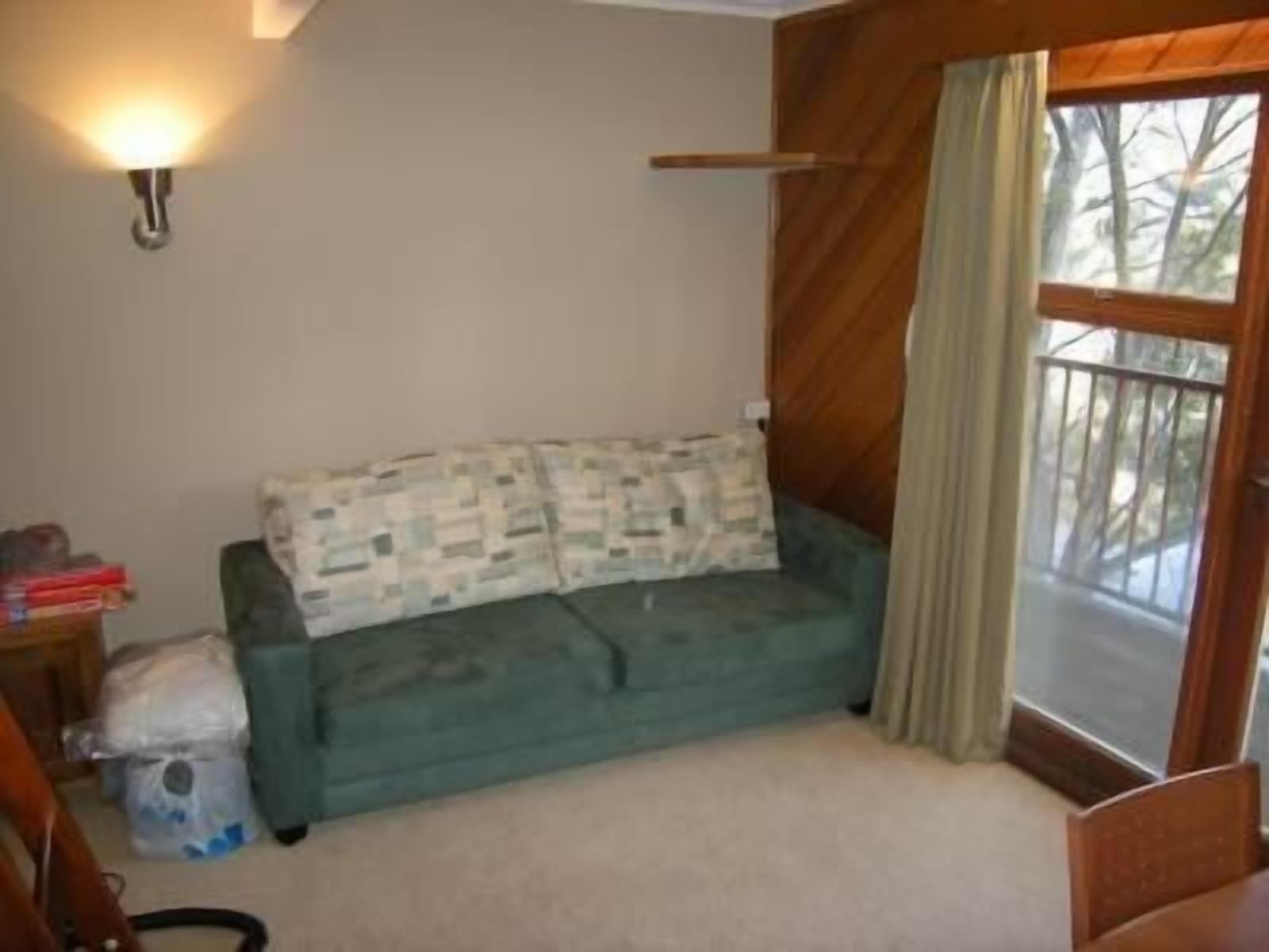 A room with a green sofa, a wooden floor, a window with curtains, and a wall-mounted light fixture.