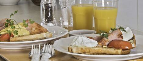 A breakfast tray with toast, eggs, and ham, accompanied by two glasses of orange juice and a bowl of fruit.