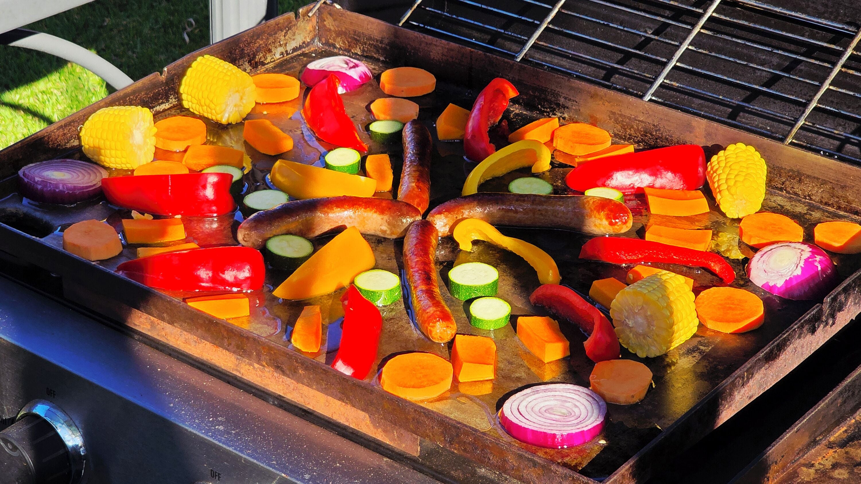 Una parrilla con diversos vegetales y salchichas a la cocción.