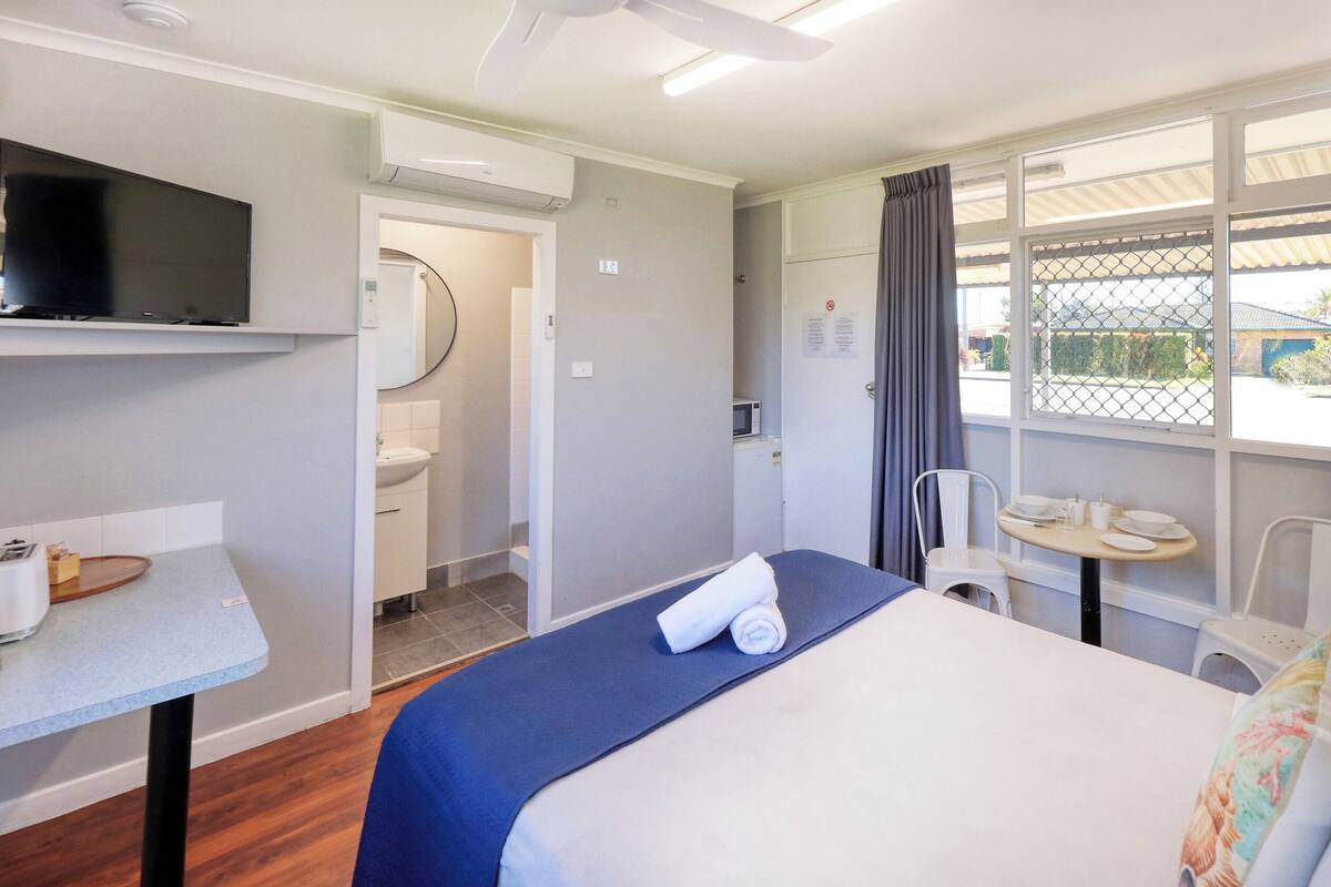 Ein Hotelzimmer mit einem Bett, einem Schreibtisch mit Wasserkocher, einer Mikrowelle, einem Fernseher und einem Fenster mit Vorhängen.