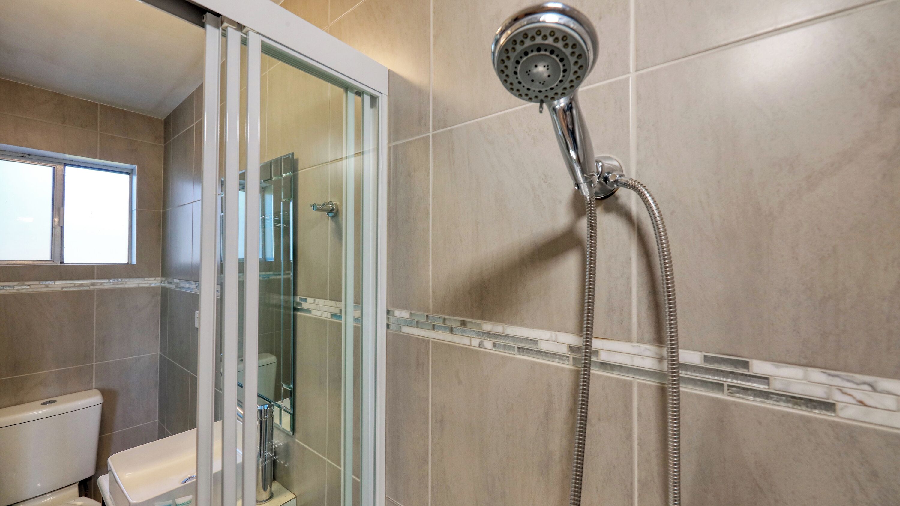 A modern bathroom with a glass shower enclosure, a toilet, and a showerhead with a flexible hose.