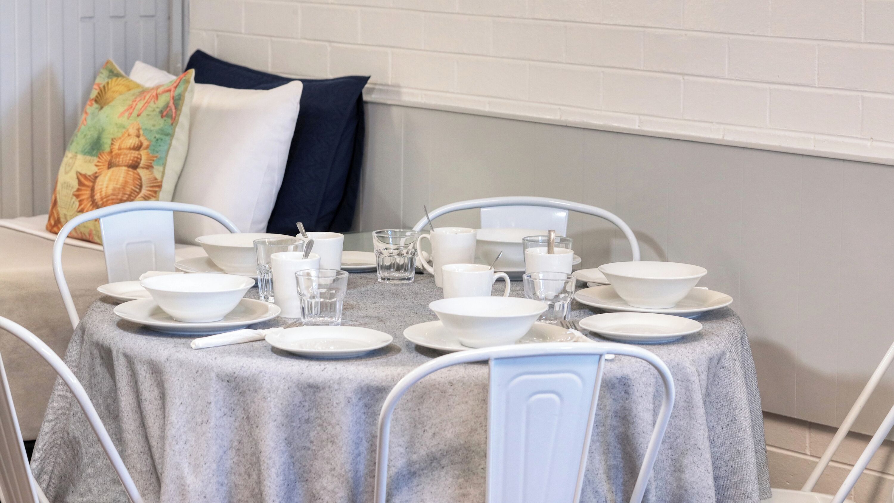 Een net gedekte eettafel met witte borden, kommen en glazen, omringd door witte stoelen.