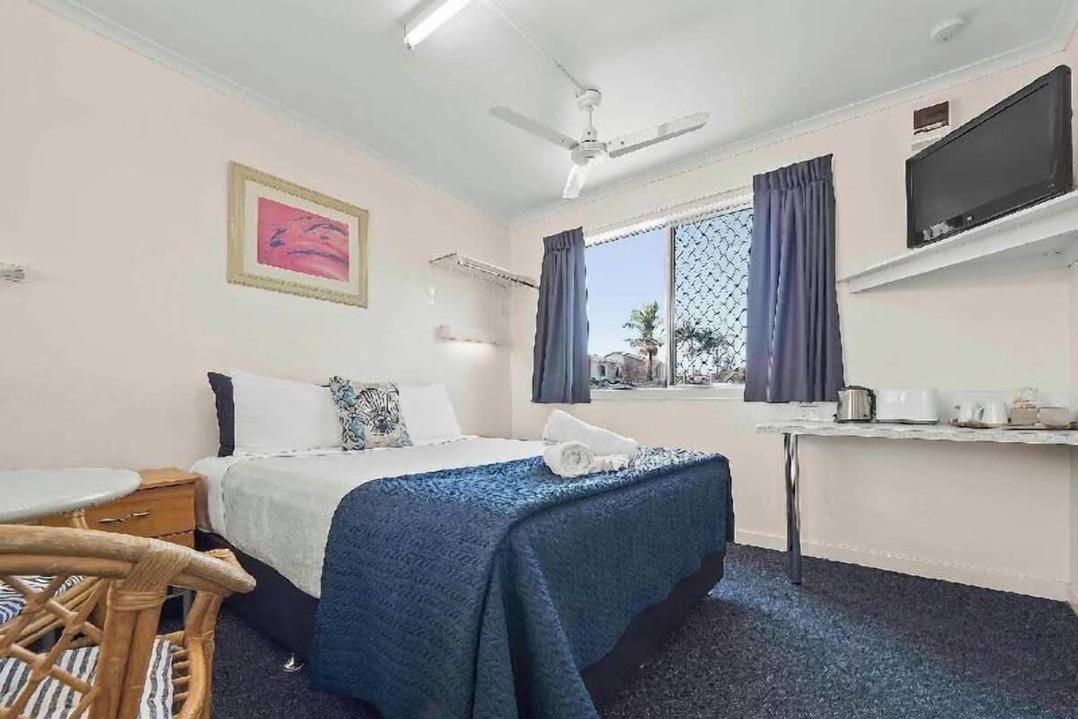 Ein Hotelzimmer mit Bett, Schreibtisch, Stuhl, Fernseher und einem fenster mit Vorhängen.