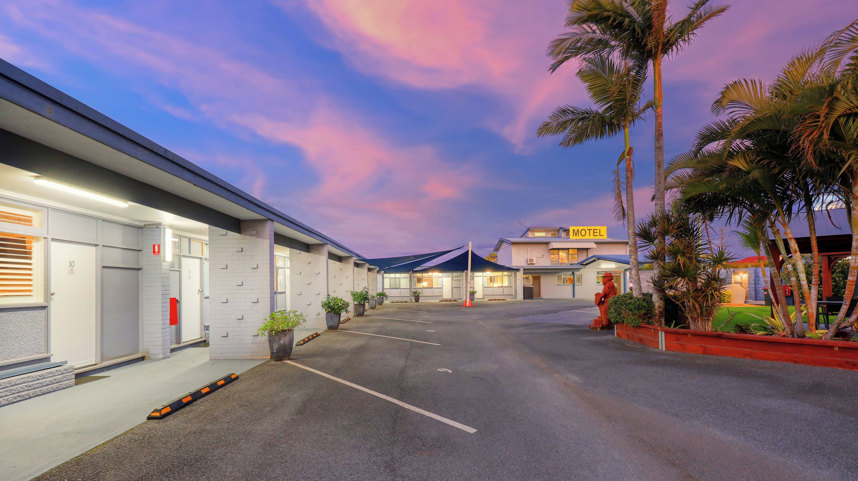 A motel with a parking lot, a building with a 'Motel' sign, and palm trees.