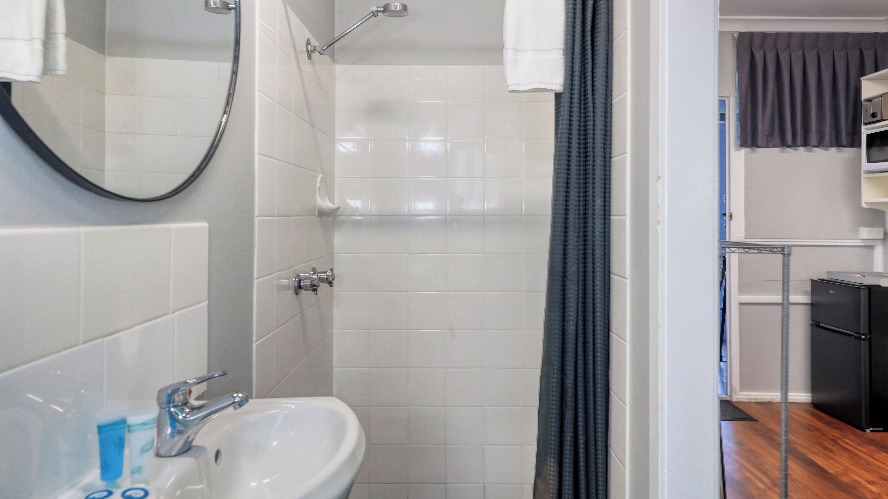 A bathroom with a white sink, a shower, and a mirror. There is a black appliance in the corner.