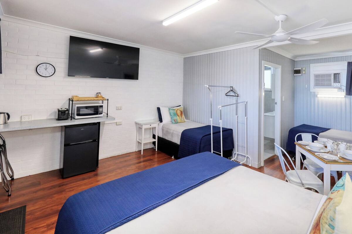 Ein Hotelzimmer mit Bett, Schreibtisch mit Mikrowelle, Fernseher und Deckenventilator.
