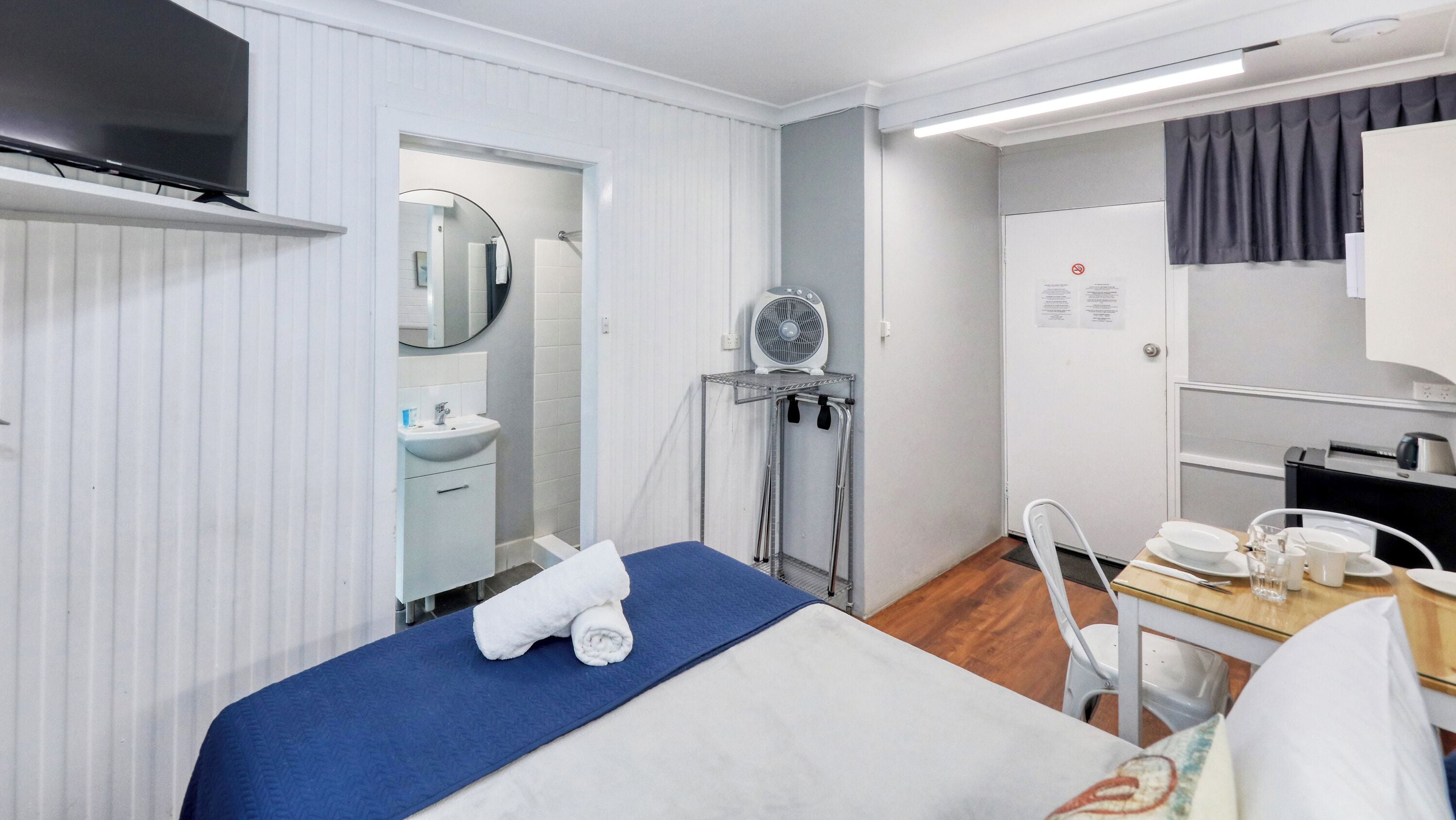 A hotel room with a bed, a sink, a mirror, a fan, and a desk with a telephone and a coffee maker.