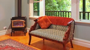 Una habitación acogedora con un sofá de madera, un estufa de leña antigua y un ventanal con vistas al verdor.