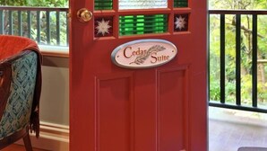 Una puerta roja con un cartel de Cedar Suite, una ventana con persianas verdes y un balcón con barandilla.