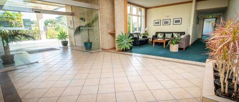 A spacious lobby with a tiled floor, a reception area with a sofa and chairs, and potted plants.