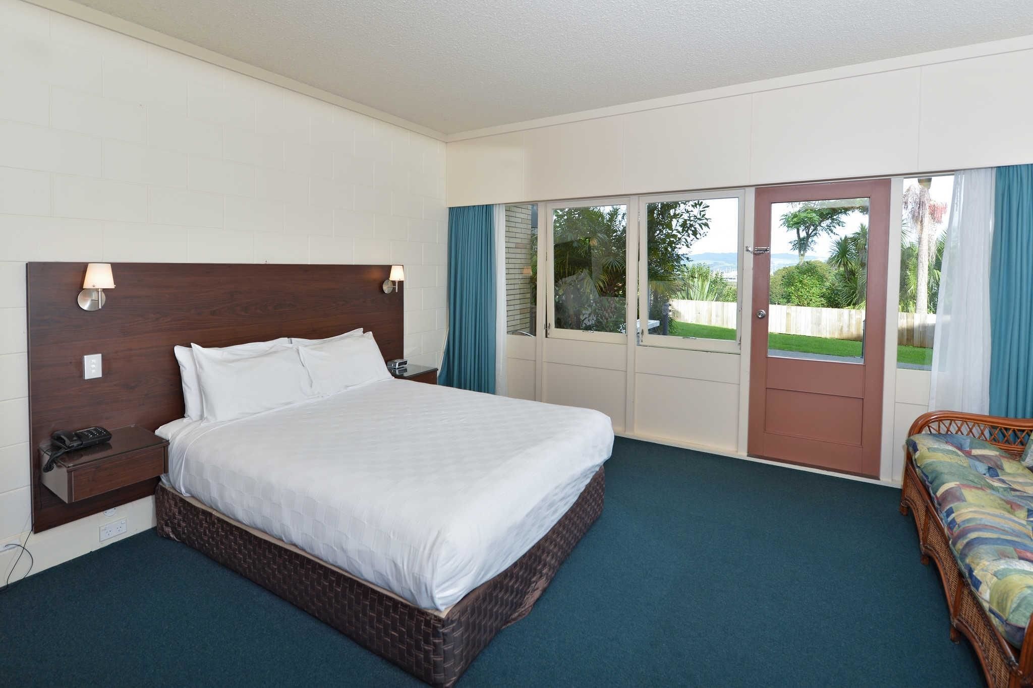 A bedroom with a large bed, a nightstand, a telephone, and a sliding door leading to a balcony.