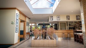 Un vestíbulo amplio con techo alto, un jardín interior central con plantas, una zona de bar con taburetes y una escalera a la vista.
