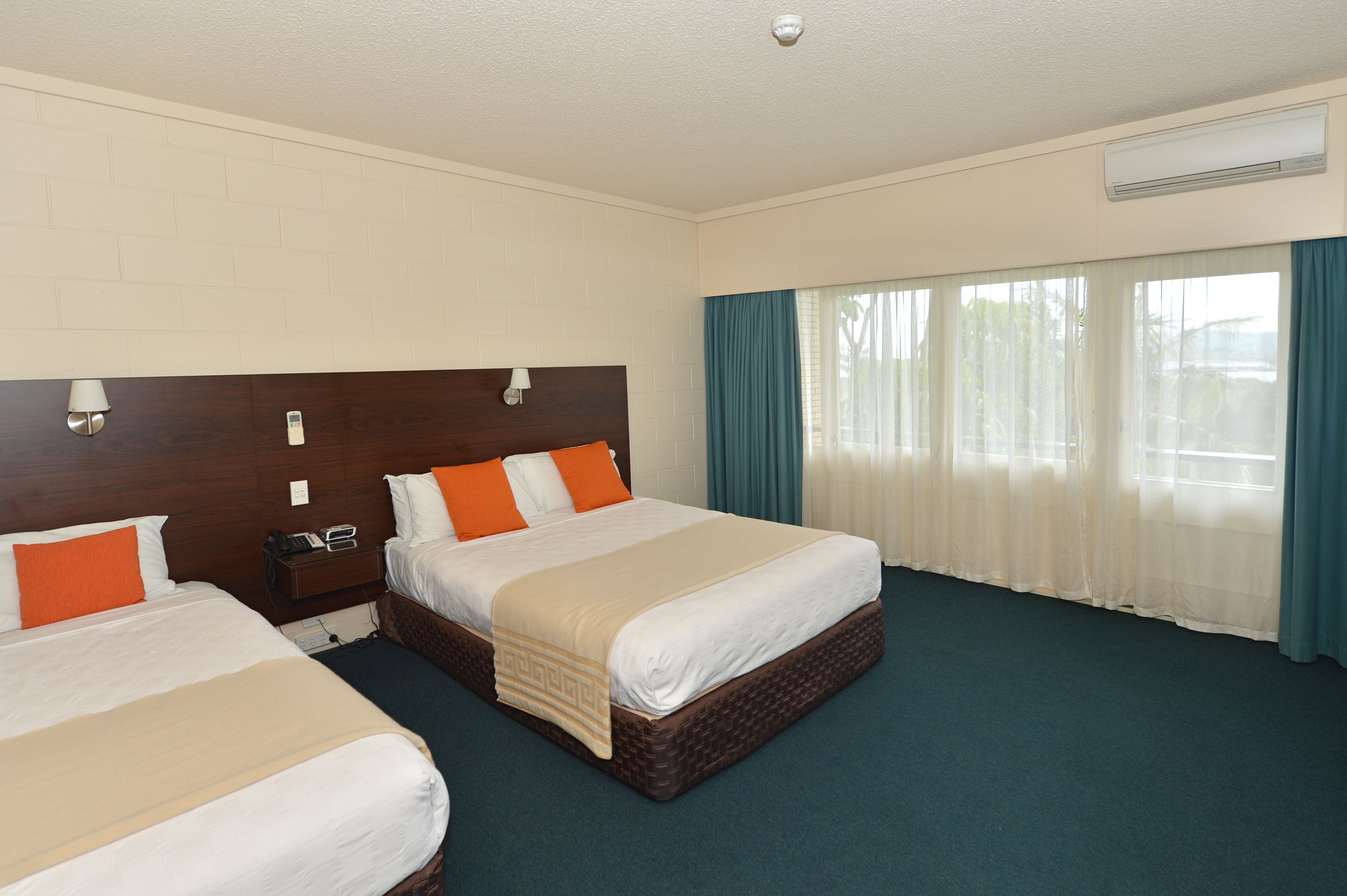 A hotel room with two beds, a wooden headboard, a nightstand, a telephone, and a window with curtains.
