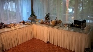 Una mesa de vidrio cubierta con un mantel blanco exhibe una variedad de alimentos y bebidas en estilo bufé.