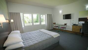 Una habitació d'hotel amb un llit, una taula de nit, una cadira, un televisor i una finestra amb cortines.
