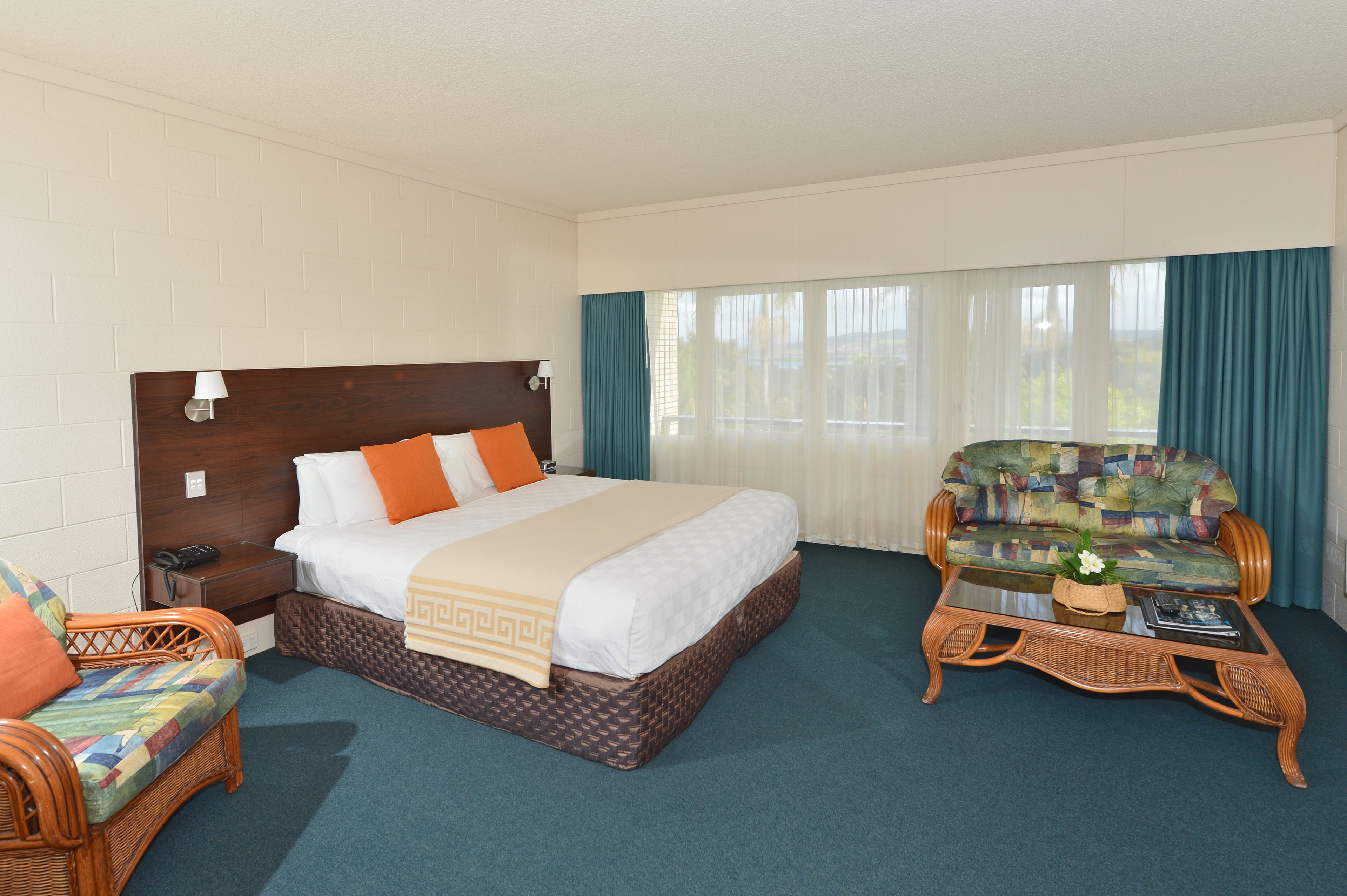 A hotel room with a large bed, a wicker armchair, a small sofa, and a coffee table.