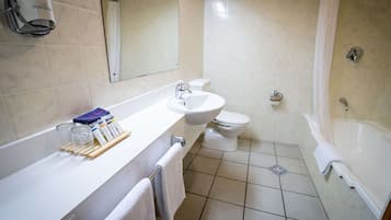 A modern bathroom with a white sink, toilet, and bathtub. There is a mirror above the sink and a towel rack with towels.