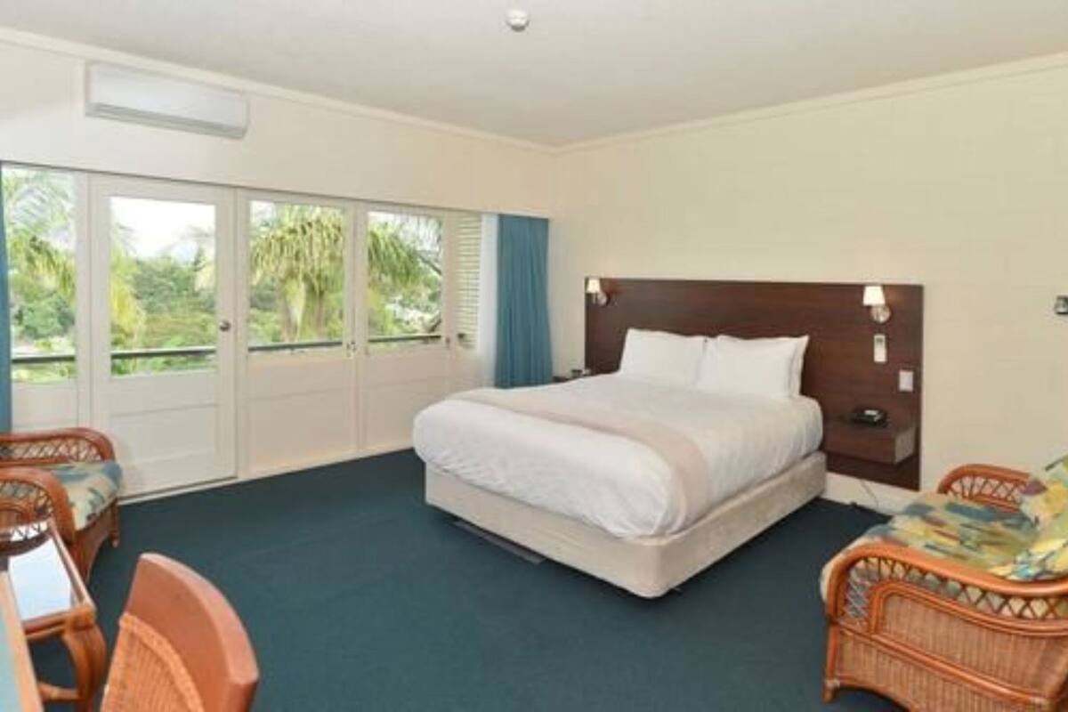 A hotel room with a bed, a desk, a chair, and a view of greenery through the door.