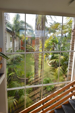 A view from a window with a wooden staircase leading to a balcony, overlooking a lush garden with various tropical plants and a building in the background. - Comfort Hotel Flames Whangerei (Whangarei)
