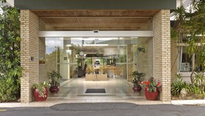 Entrada de hotel con diseño moderno, destacando fachada de ladrillo, puertas de cristal y plantas en macetas.