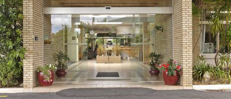 A hotel entrance with a modern design, featuring a brick facade, glass doors, and potted plants.
