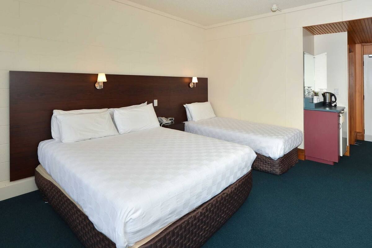 A hotel room with two beds, a wooden headboard, a small kitchenette, and a mirror.