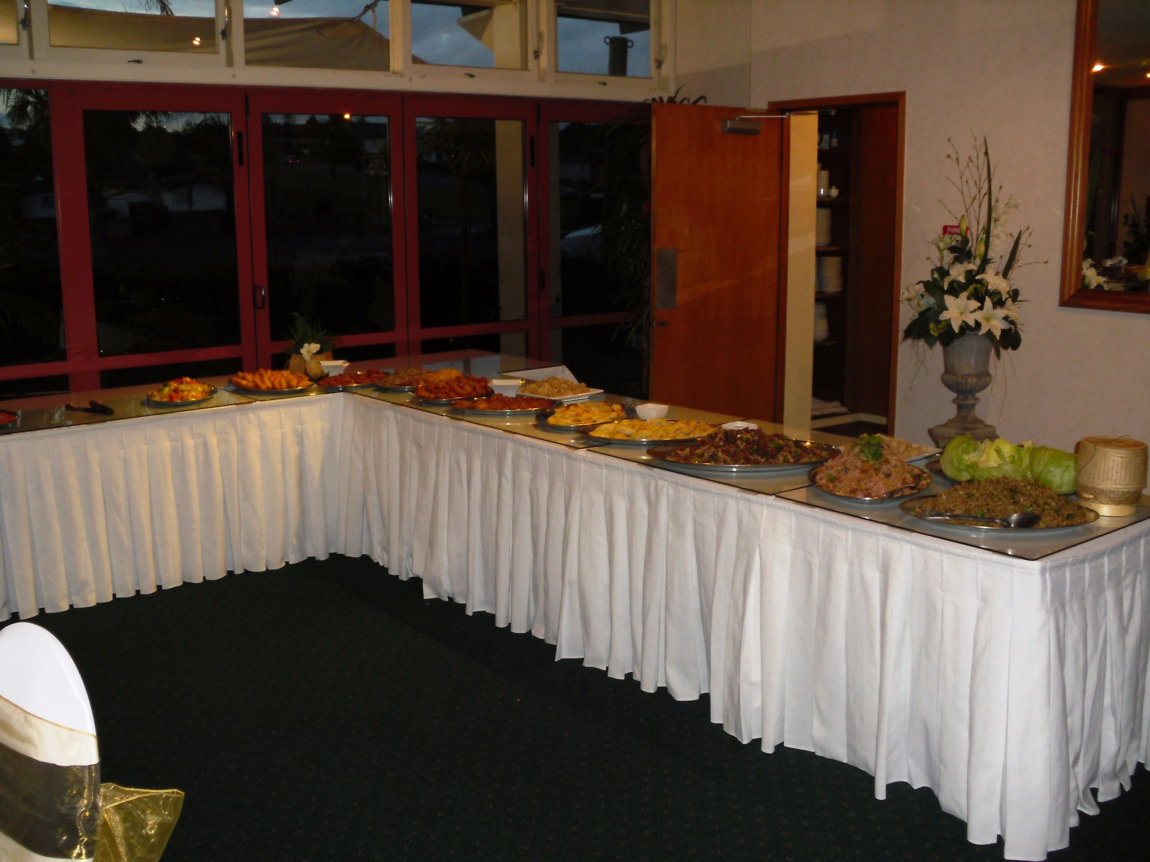A buffet table with various dishes, a vase of flowers, and a fire extinguisher on the wall.