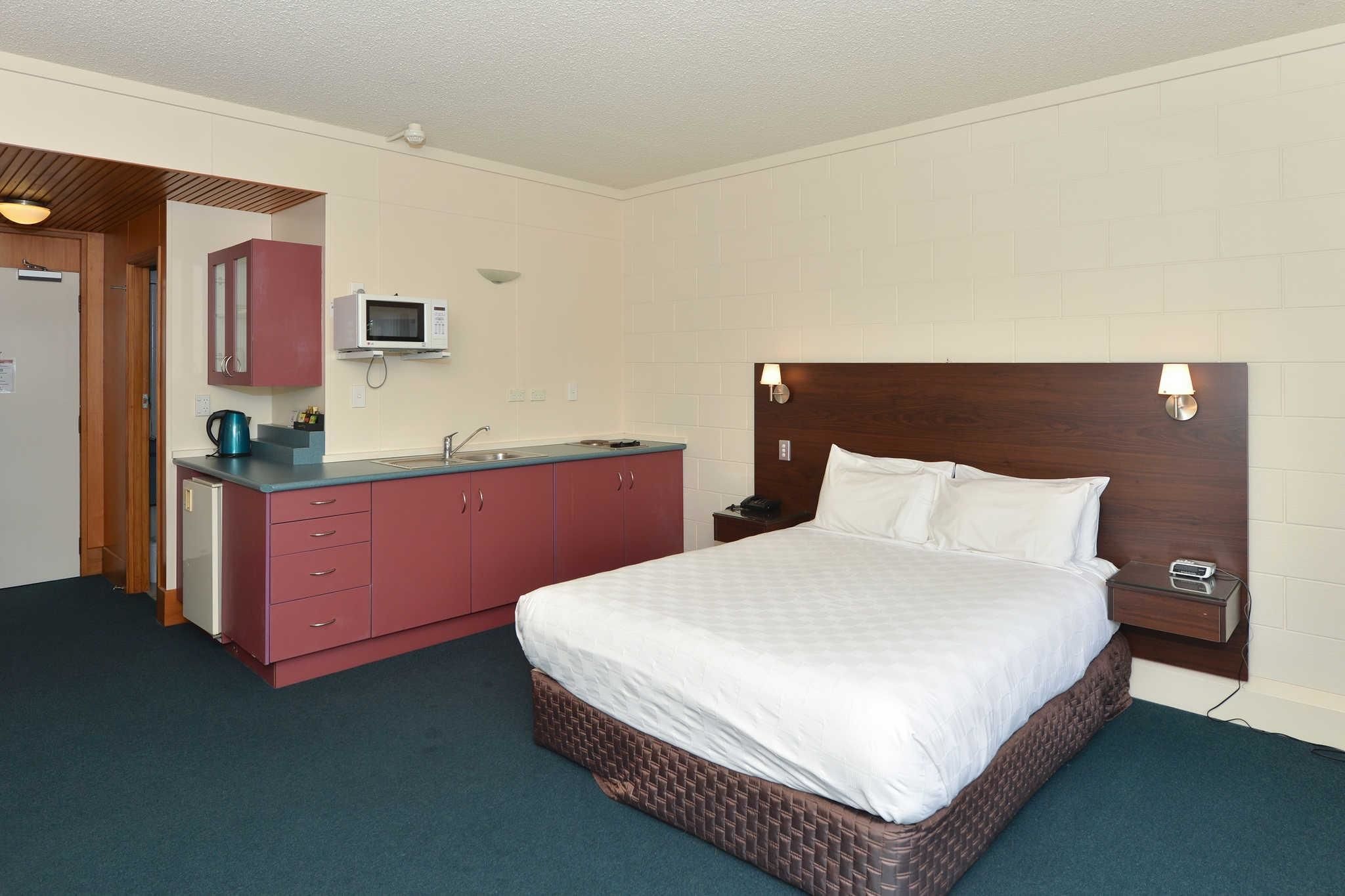 Een hotelkamer met een bed, een kleine kitchenette, een magnetron en een nachtkastje.