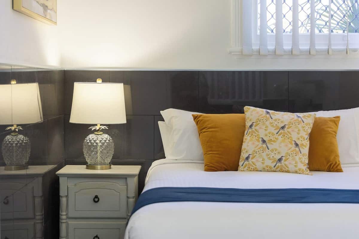 A neatly arranged hotel room with a bed, two bedside tables with lamps, a window with a view, and a wall-mounted artwork.