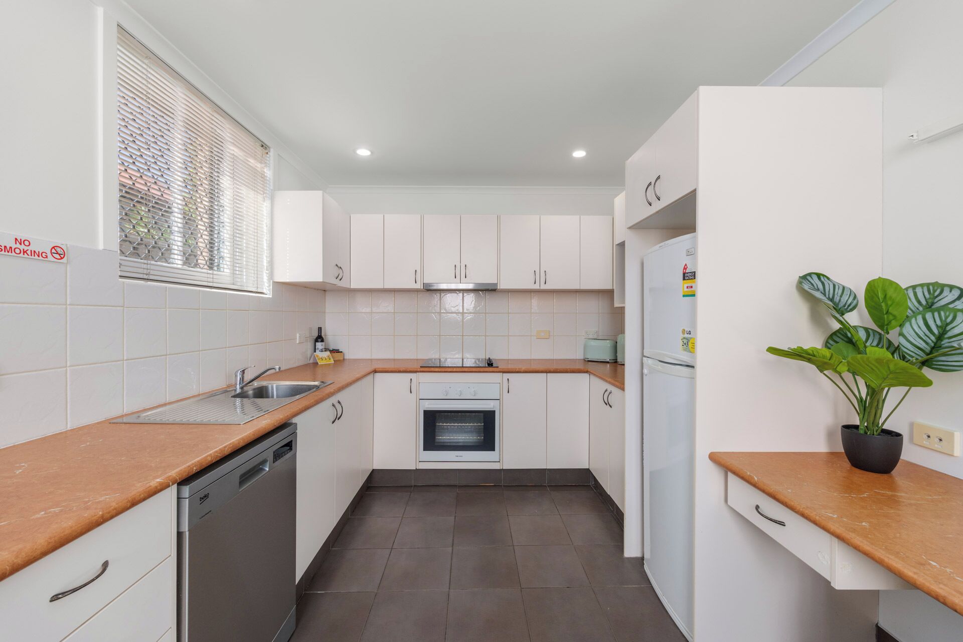 Una cocina moderna con armarios blancos, lavavajillas, horno y refrigerador.