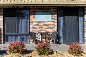 A brick building with a sign for 'Charlestown on the Park' self-contained holiday accommodation, a patio with chairs, and a small garden. - Charlesworth On The Park (Glen Innes)