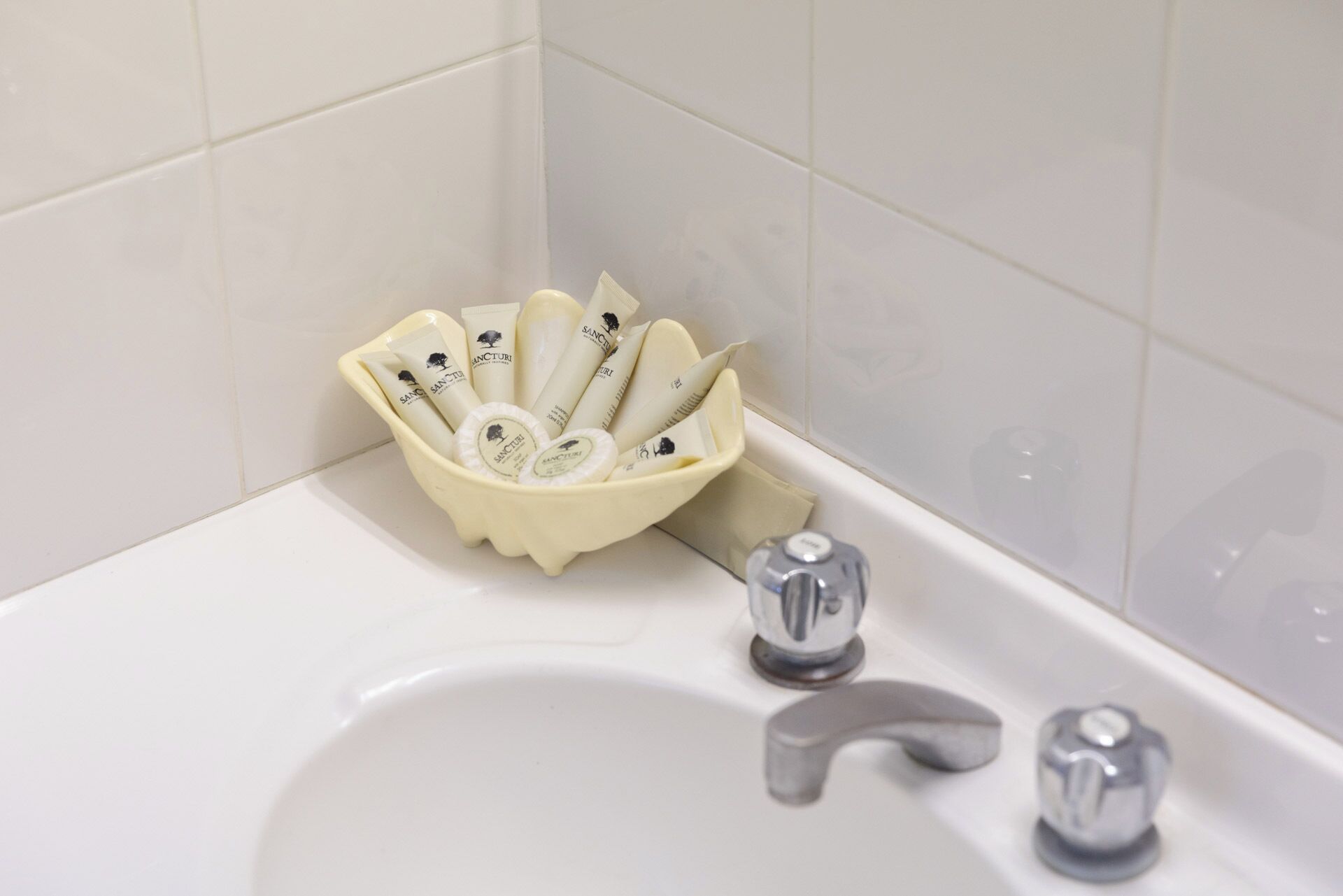 A bathroom sink with a beige basin containing toiletries and a bottle of hand soap.