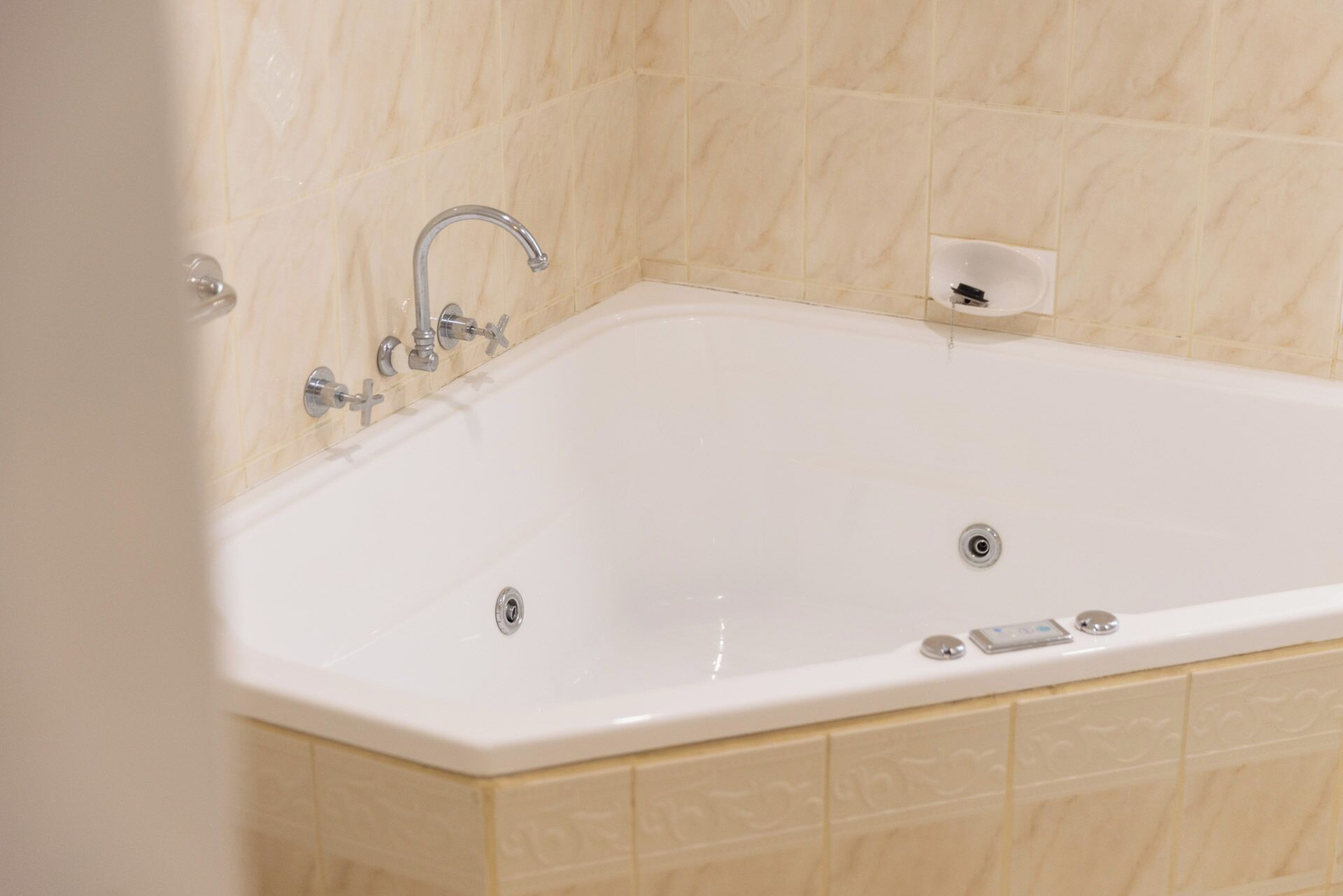 A white bathtub with a single faucet, a handheld showerhead, and a control panel.