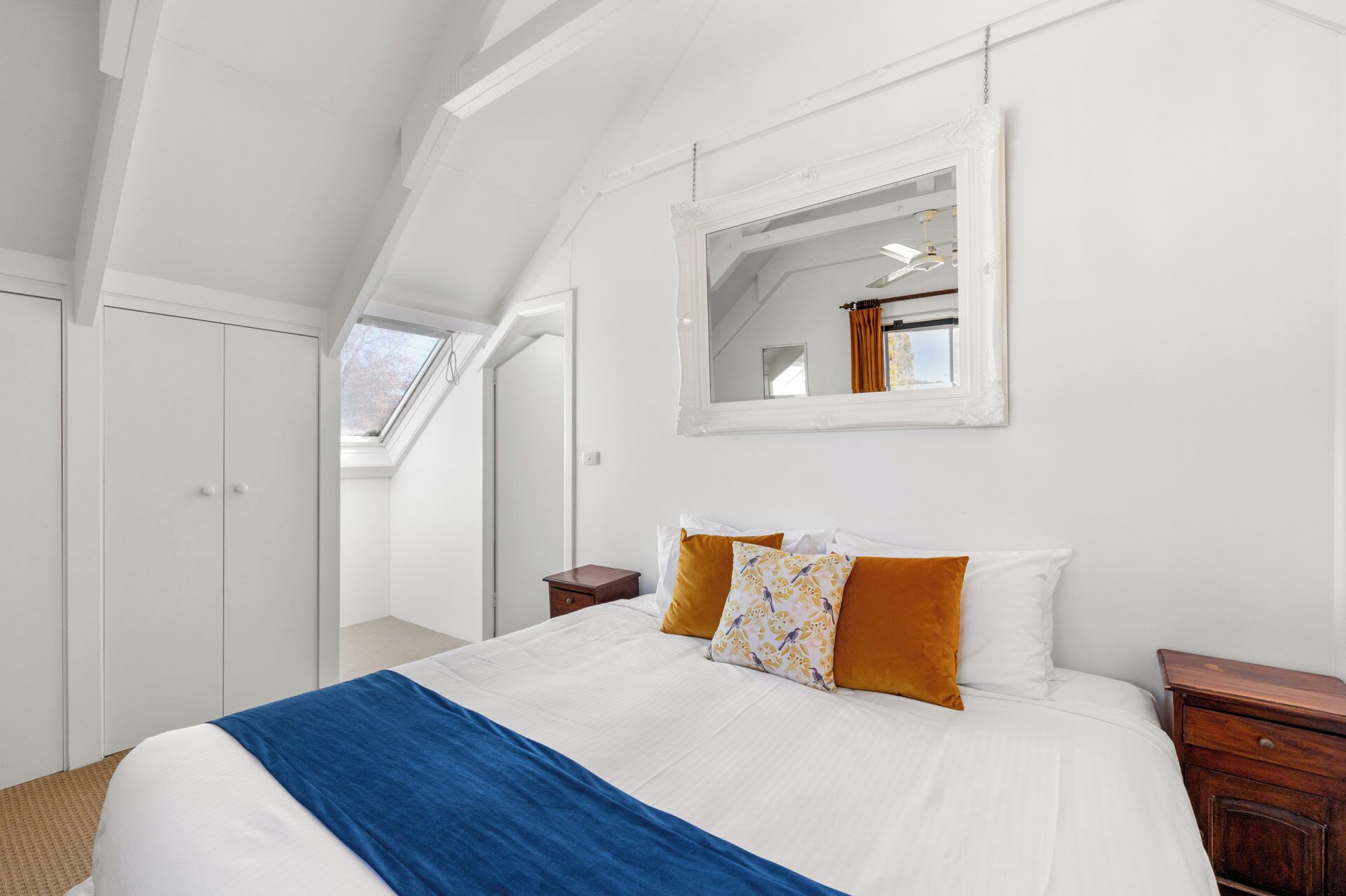 Un dormitorio con una cama grande, tragaluz, espejo y armario.