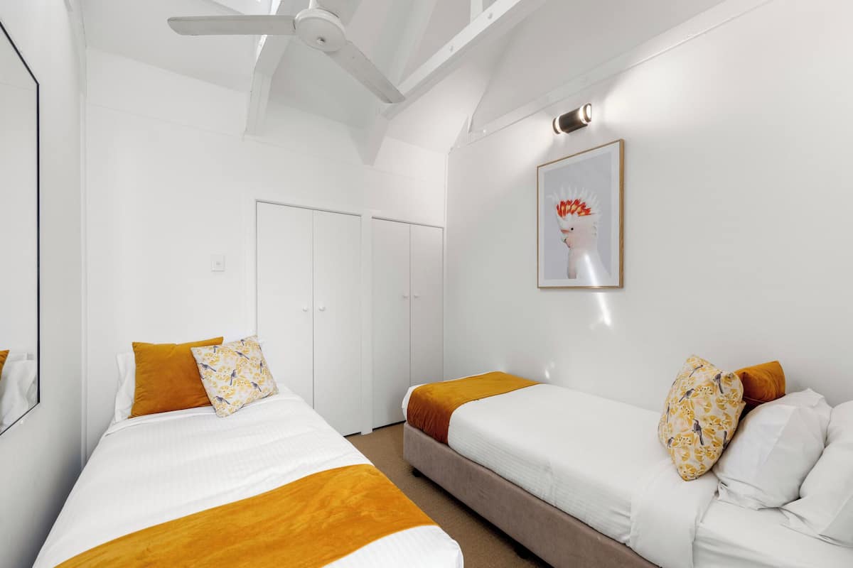 A hotel room with two beds, a ceiling fan, a door, and a framed picture on the wall.