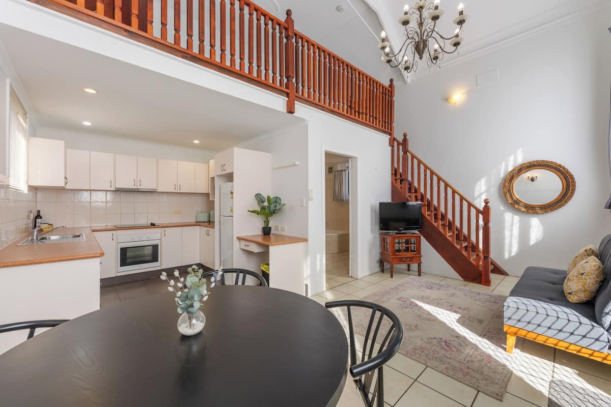 A spacious living area with a dining table, chairs, a sofa, a staircase, a kitchen, and a TV.