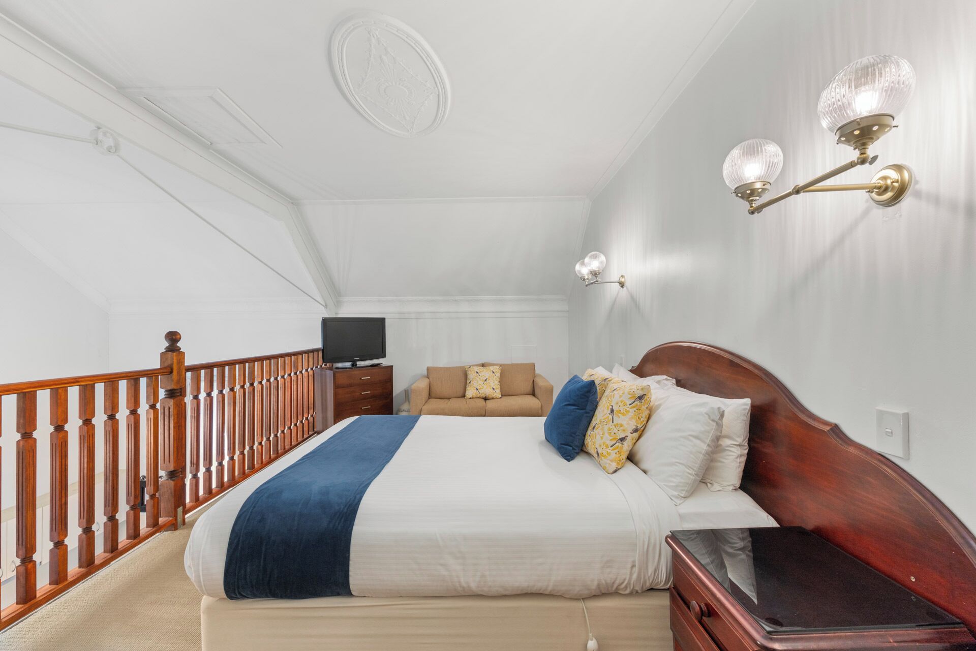 Une chambre à coucher avec un lit en bois, un téléviseur, une table de chevet et un luminaire fixé au mur.