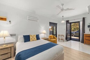 Ein Hotelzimmer mit Bett, Nachttischlampen, Deckenventilator, Fenster mit Aussicht und einem Essbereich mit Tisch und Stühlen.