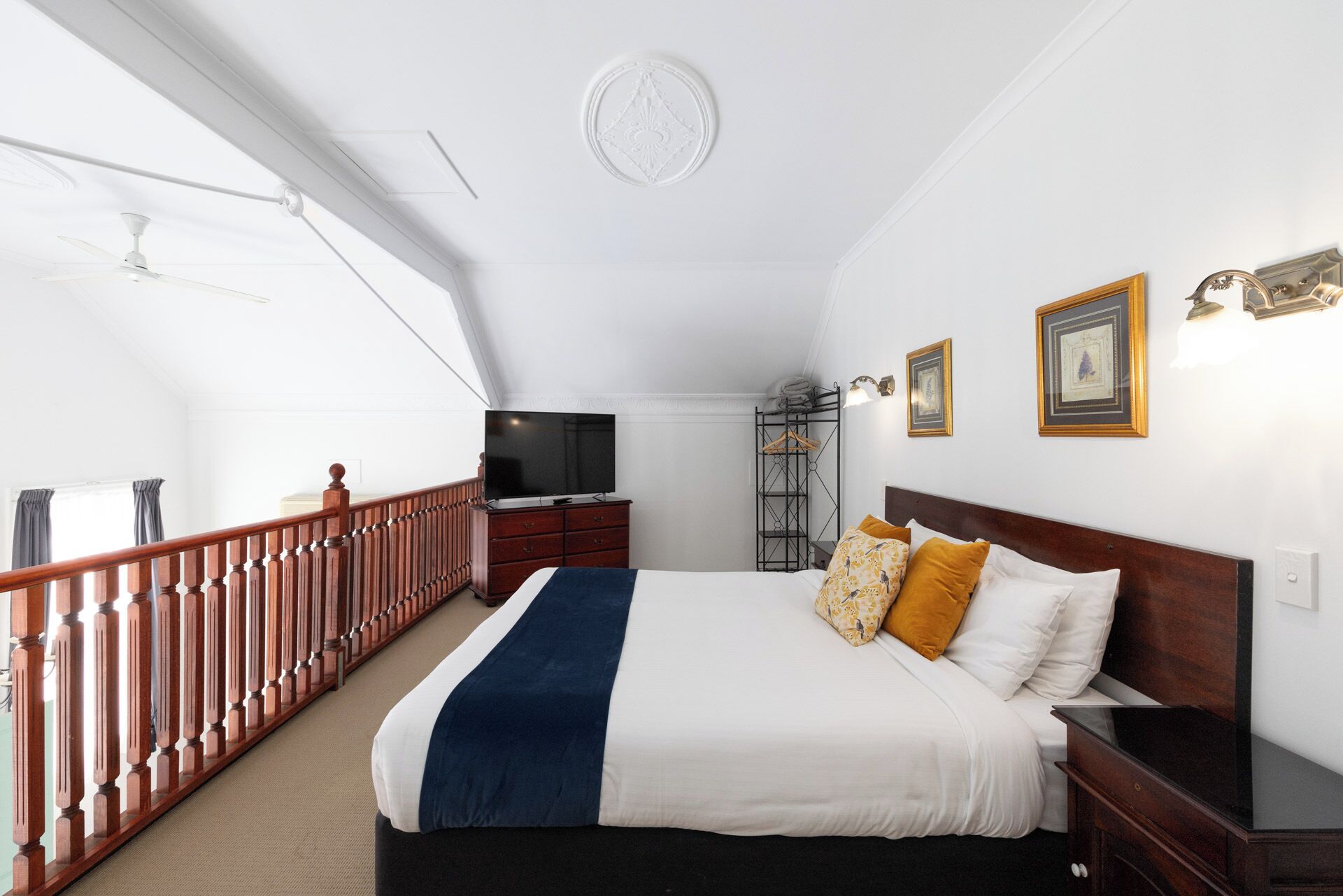 A hotel room with a bed, a TV, a wooden railing, a wardrobe, and framed pictures on the wall.
