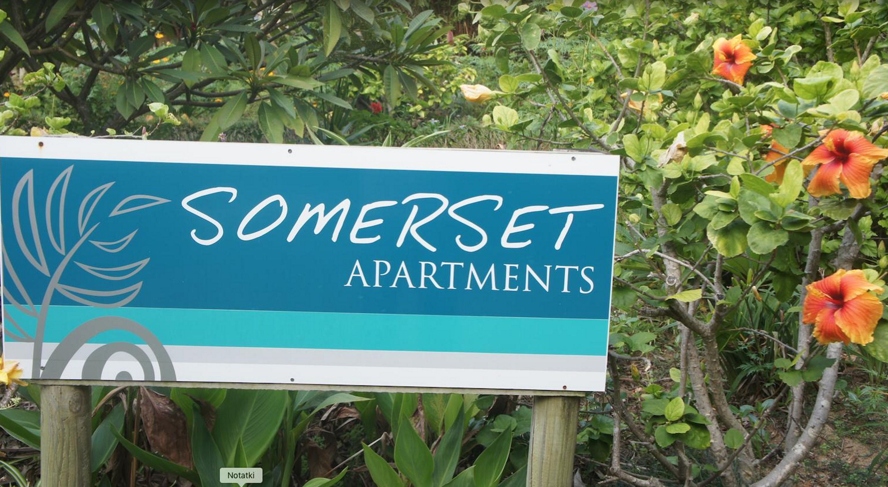 A sign for Somerset Apartments with a simple layout and a natural backdrop.