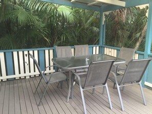 Eine überdachte Terrasse im Freien mit Tisch und Stühlen, umgeben von einer Holzterrasse und einem weißen Zaun.