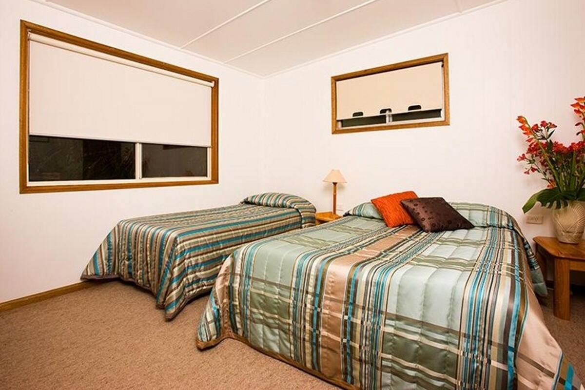 A bedroom with two single beds, a nightstand, a lamp, a mirror, and a window.