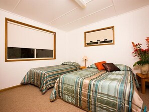 A bedroom with two single beds, a nightstand, a lamp, a mirror, and a window. - Somerset Apartments Lord Howe Island (Lord Howe Island)