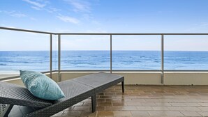 A balcony with a wicker lounge chair and a cushion, overlooking the ocean. - Foreshore Apartments (Mermaid Beach)