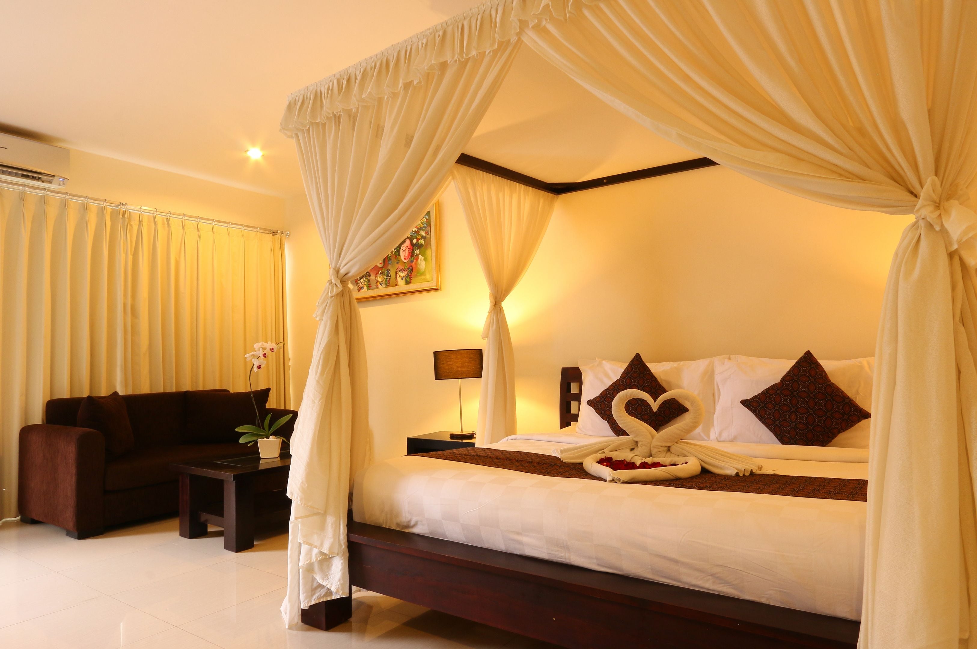 A bedroom with a canopy bed, a sofa, a small table, and a potted plant.